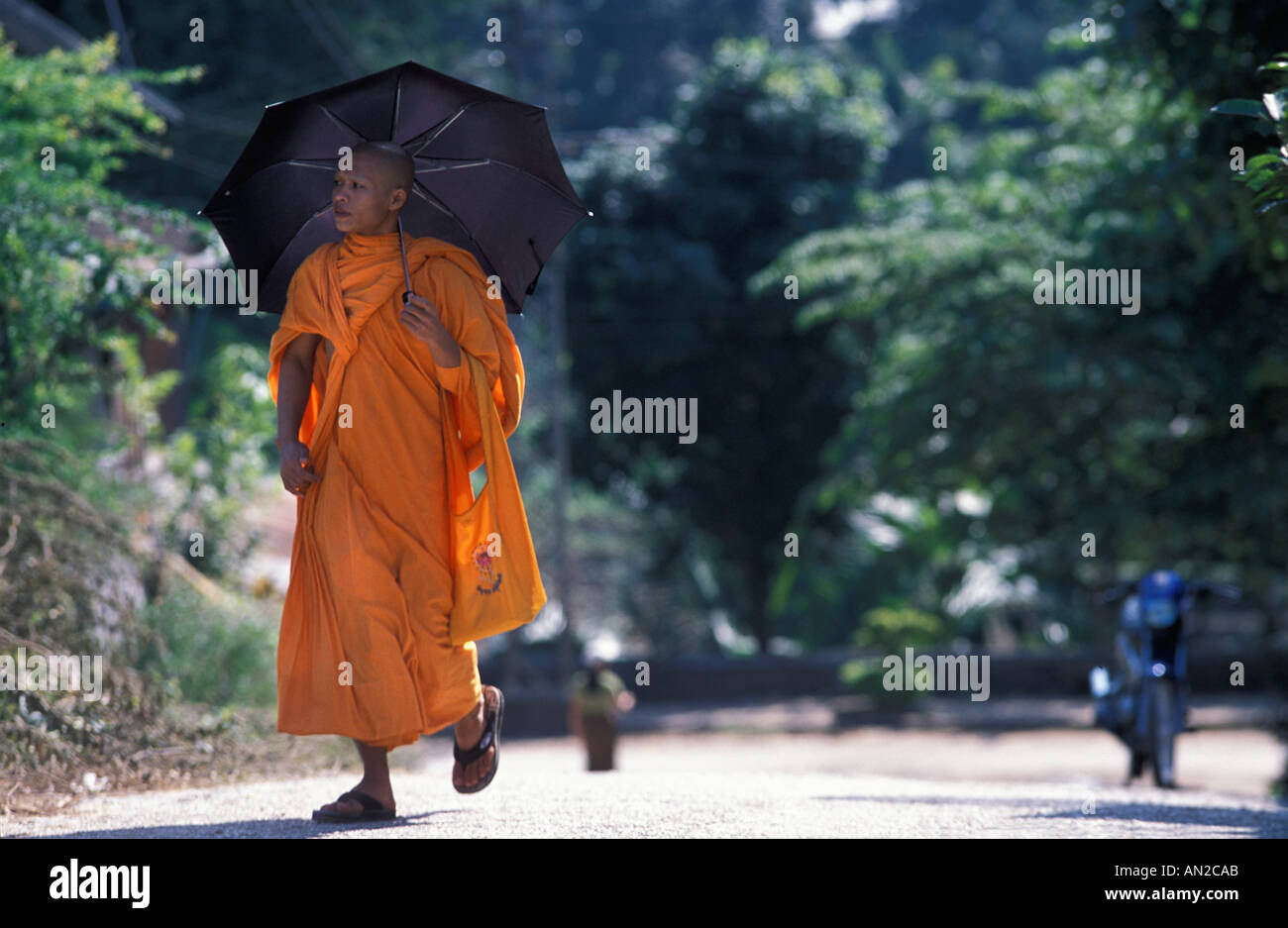 Monk with parasol umbrella shielding from the stron tropical sun Near Wat Xieng Thong Luang Prabang Laos Stock Photo