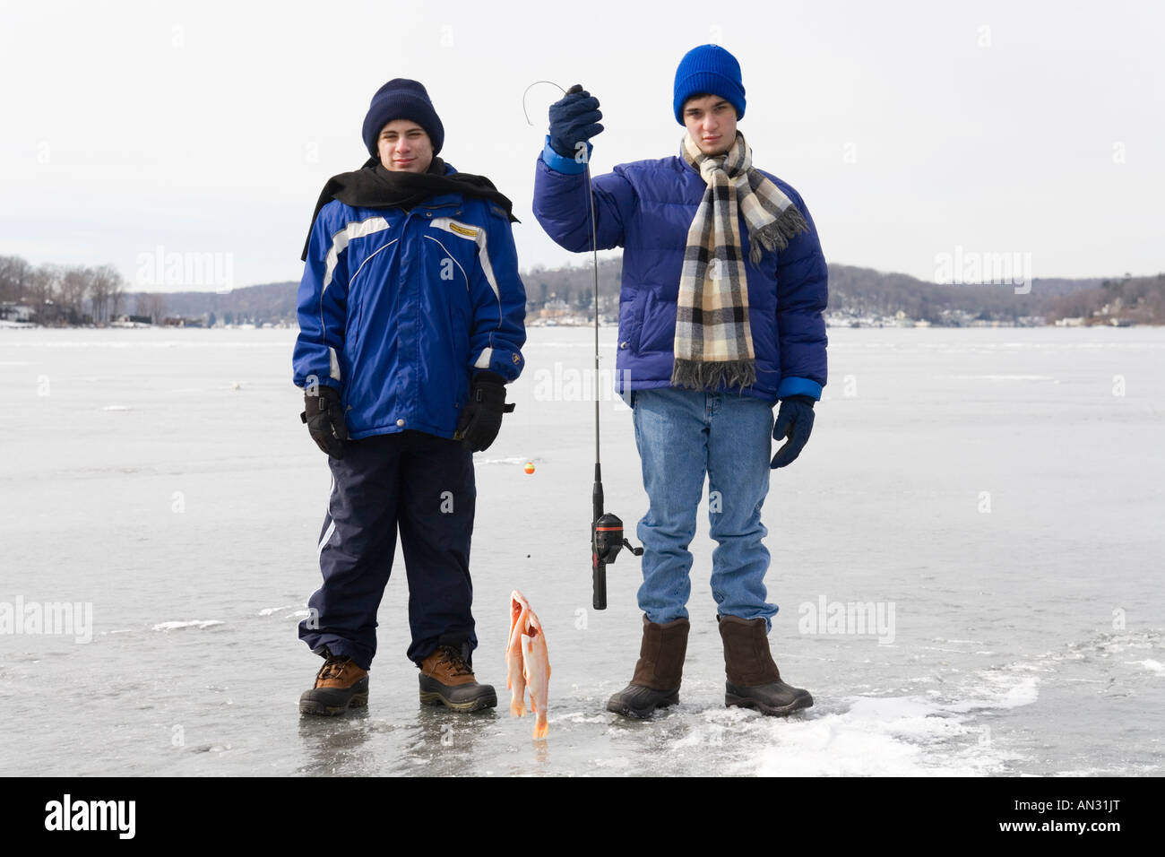 Two Teenagers standing on a frozen lake holding a fishing pole and two