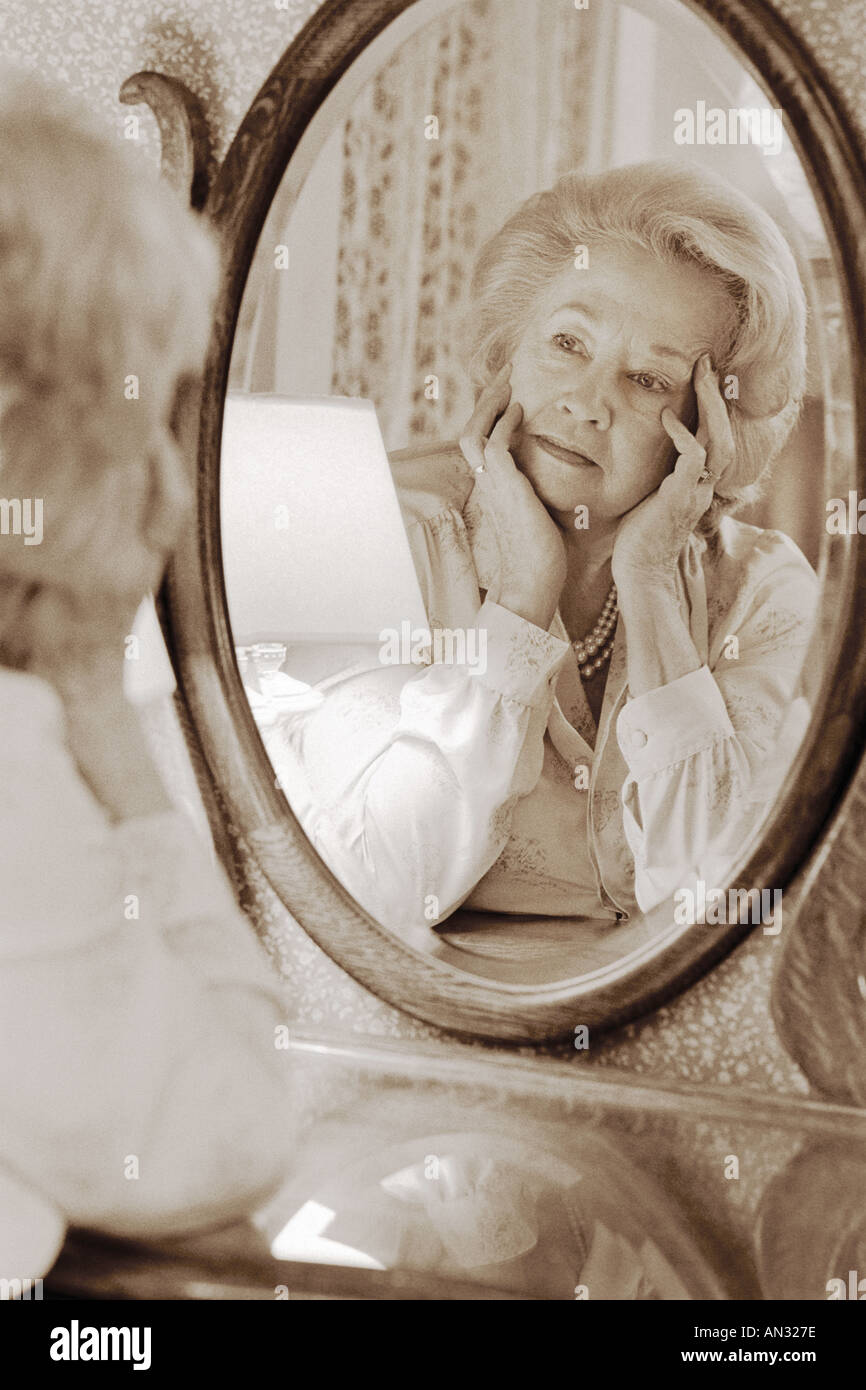 Black and white sepia image of senior woman looking in oval mirror on dressing room table Stock Photo