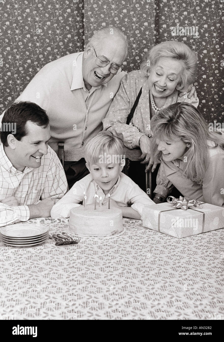 Black and white image of generational family celebrating young boy's birthday in dining room Stock Photo