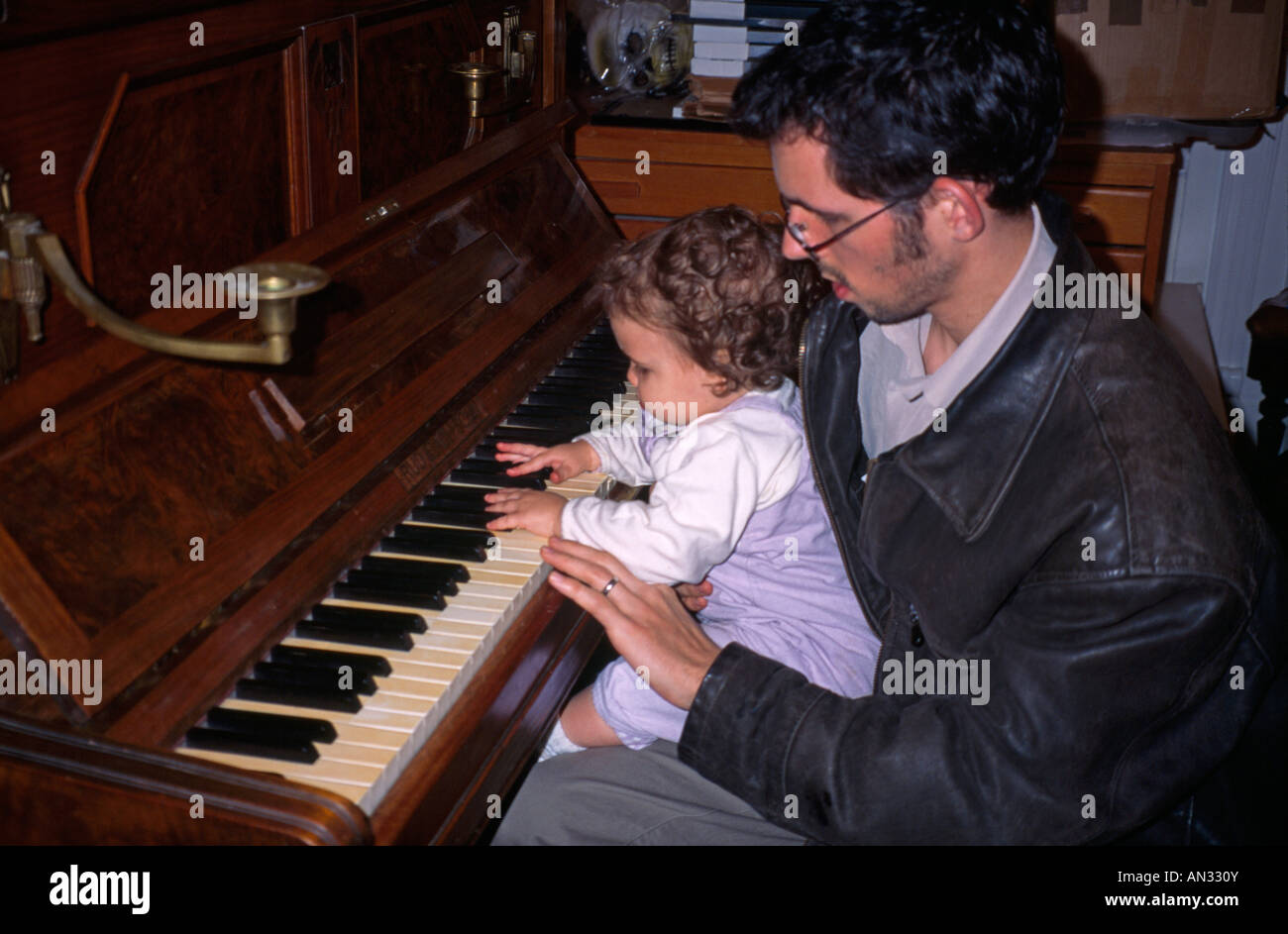 Man Looking After Baby Girl Playing At Piano Stock Photo