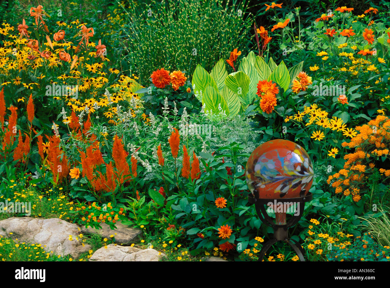 A blooming summer flower garden with a glass gazing globe of orange-yellow colors and vibrant flowers, Missouri USA Stock Photo
