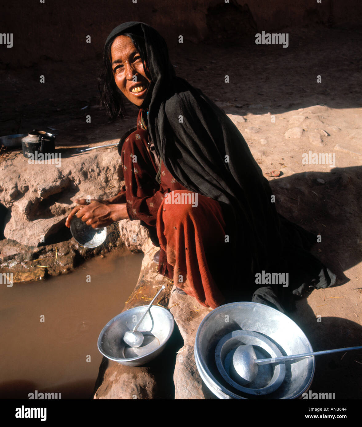 Woman washing dishes in a muddy pool of water. Stock Photo