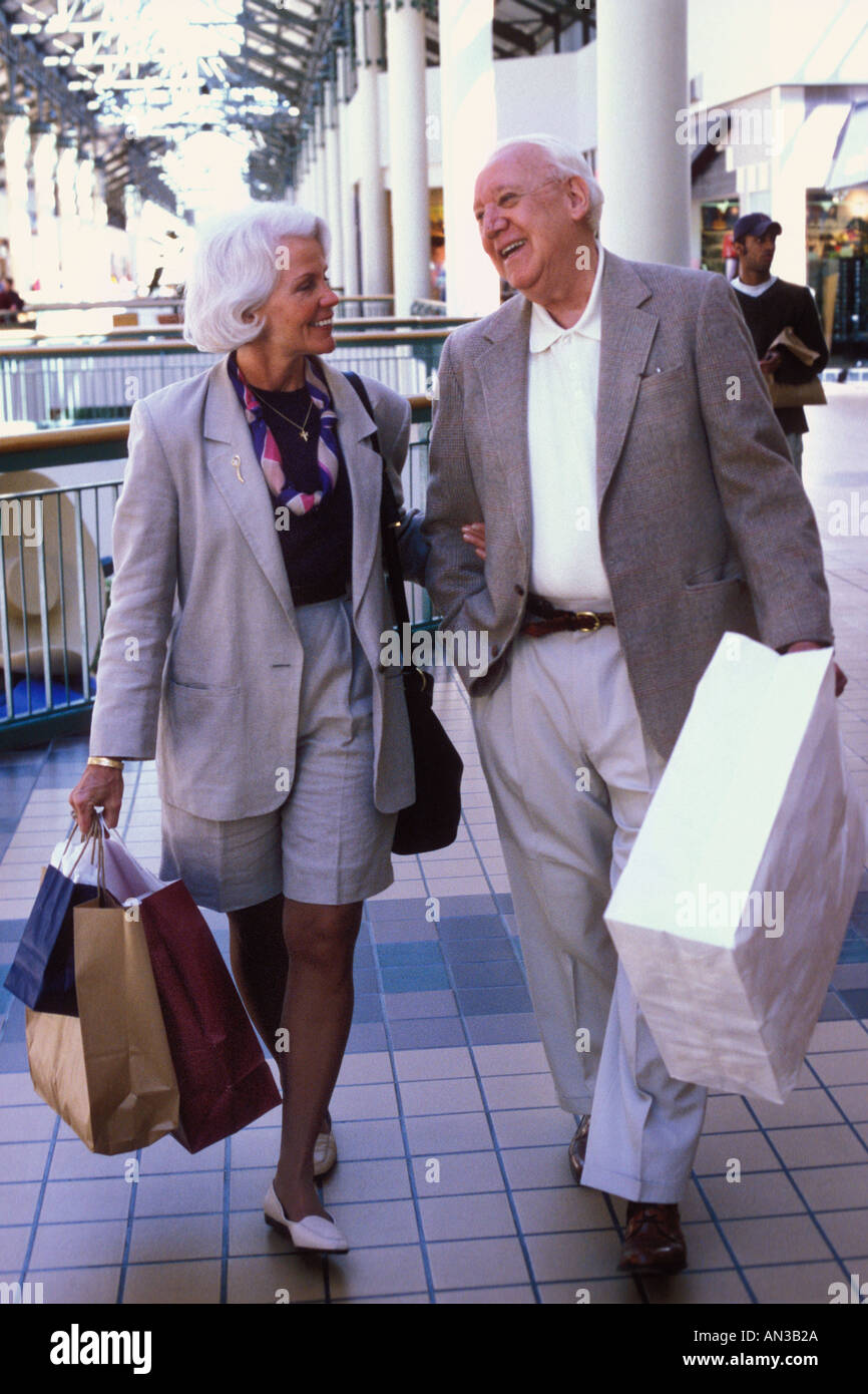 Caucasian senior couple shopping walking talking laughing with shopping bags in mall Stock Photo