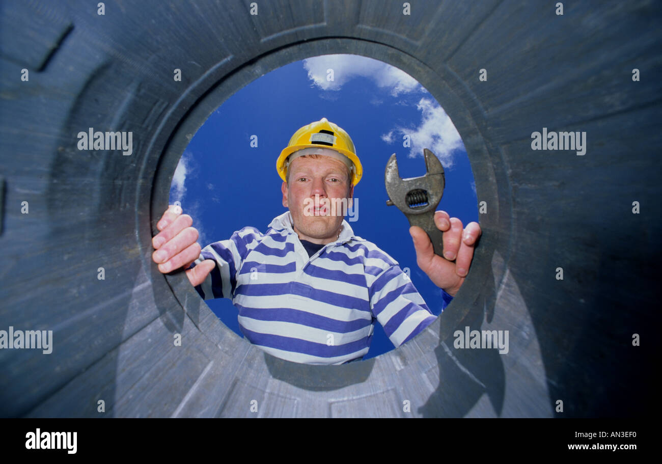 construction worker holding spanner looking through piping Stock Photo