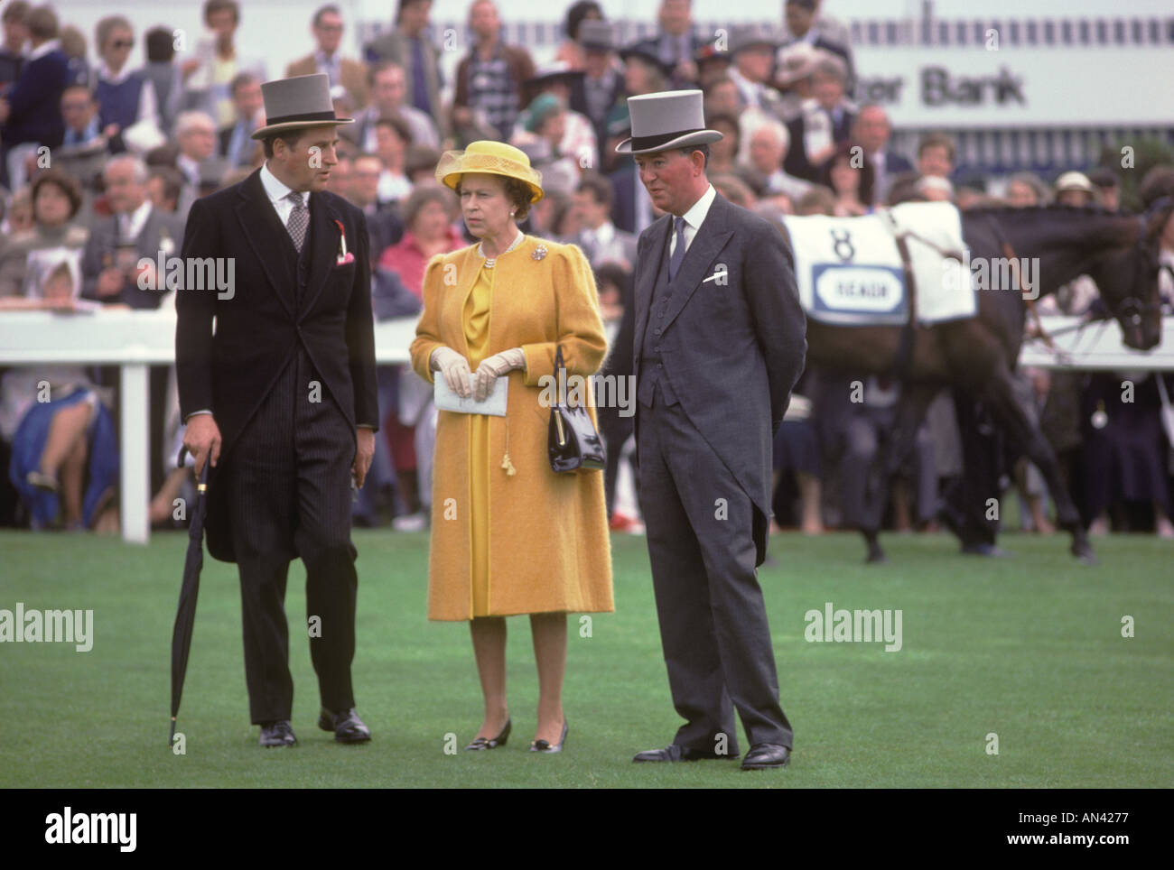 Lord Porchester the Earl Carnarvon (left) Queen Elizabeth II  in yellow dress with courtier at Derby Day horse race Epsom Downs Surrey 1984 1980s UK Stock Photo