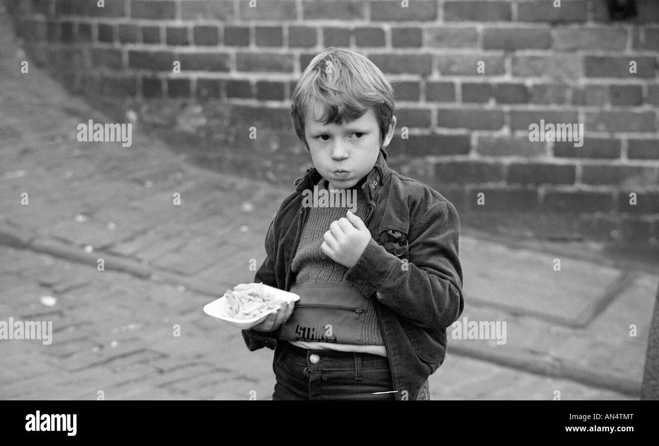 Young boy eating fish and chips from a plastic tray in the street. Stock Photo