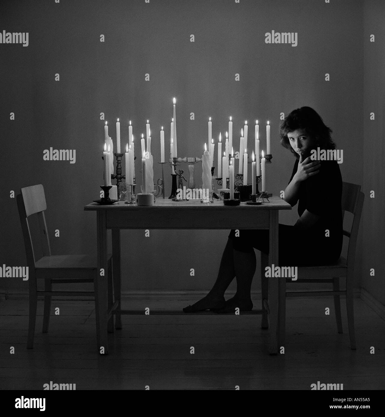 Sad woman sitting in empty room Several lit candles on table. 18, 19, 20, 20s, 20-24. 25-29, 30s years old, Stock Photo