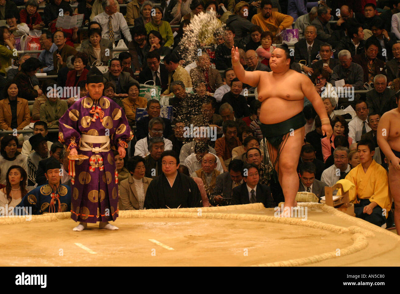 A sumo wrestler thows salt high in the air during his ritual at the