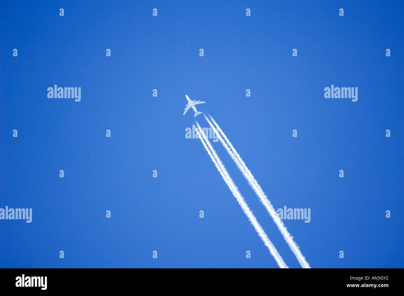 4 engined jet airplane flying from the UK  to the USA with polluting contrails vapour trails in the clear blue sky Stock Photo