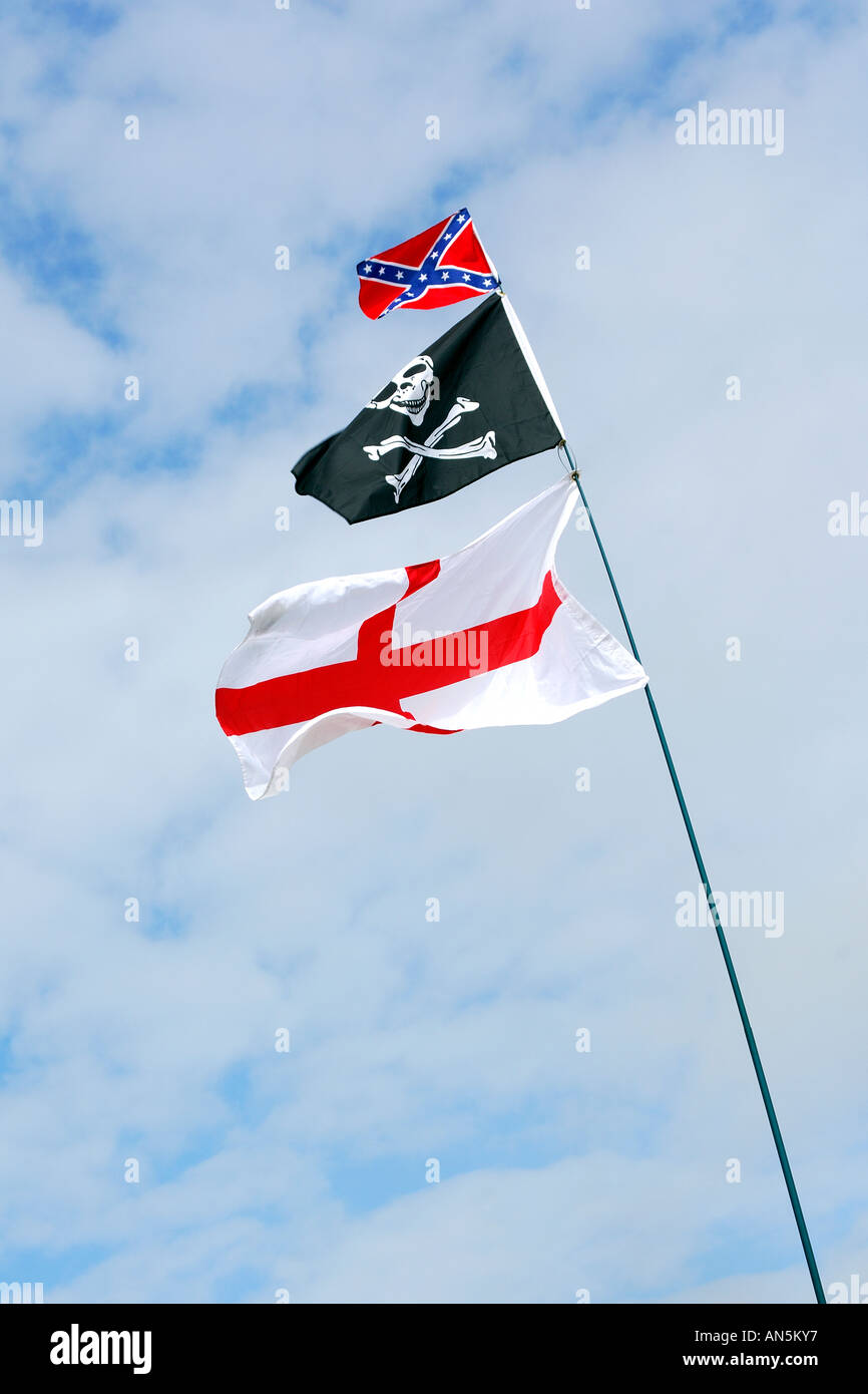 Three flags flying on a single flag pole against a blue cloudy sky flag of St George Jolly Roger and the confederate battle flag Stock Photo