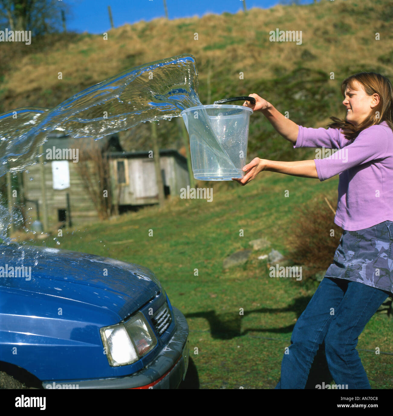 Teenage girl washing the car for pocket money allowance with a bucket of water Wales UK Stock Photo