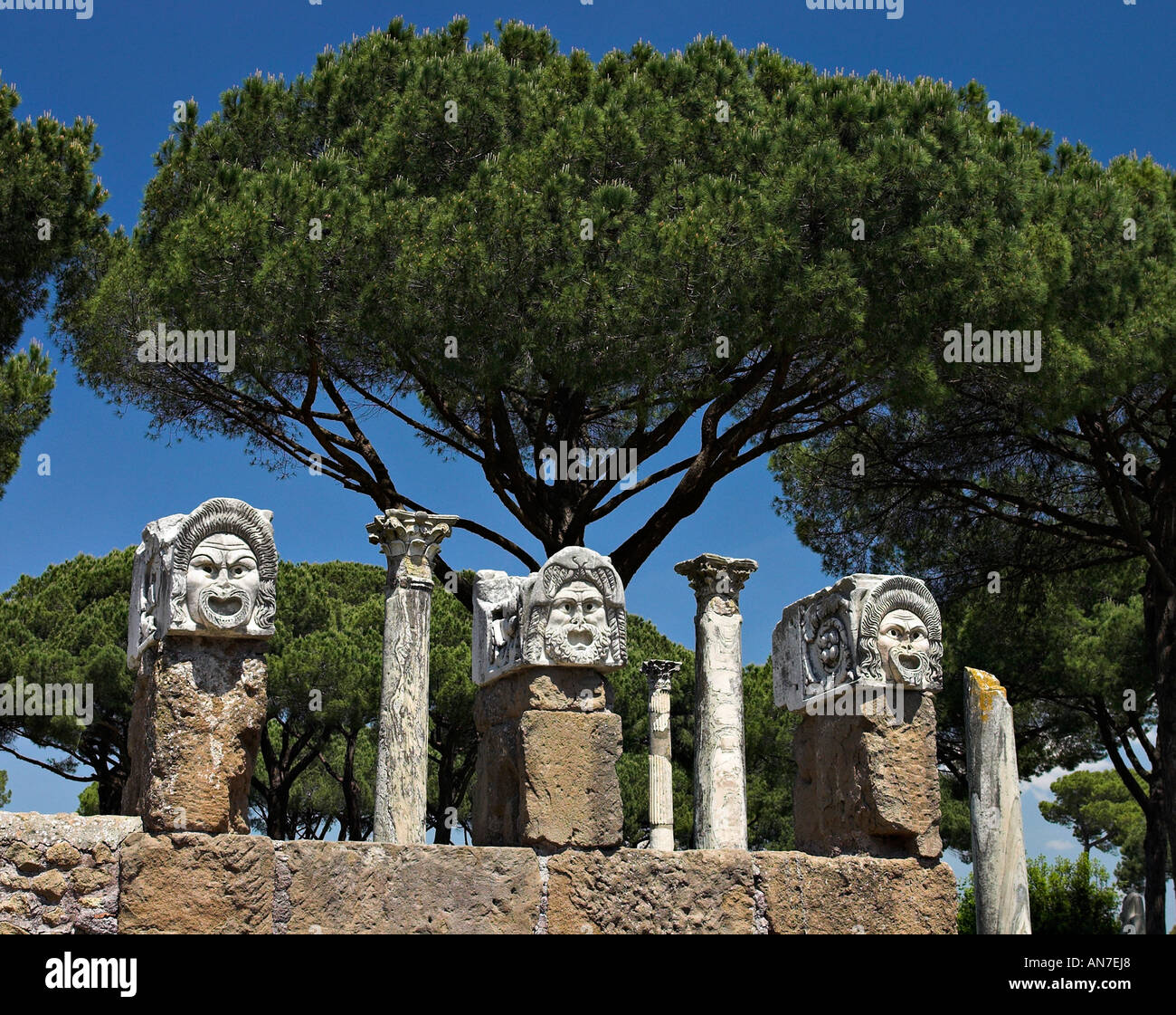 Stone Masks and Umbrella Pine. Three carved stone masks set on columns decorate and advertise the theatre Stock Photo