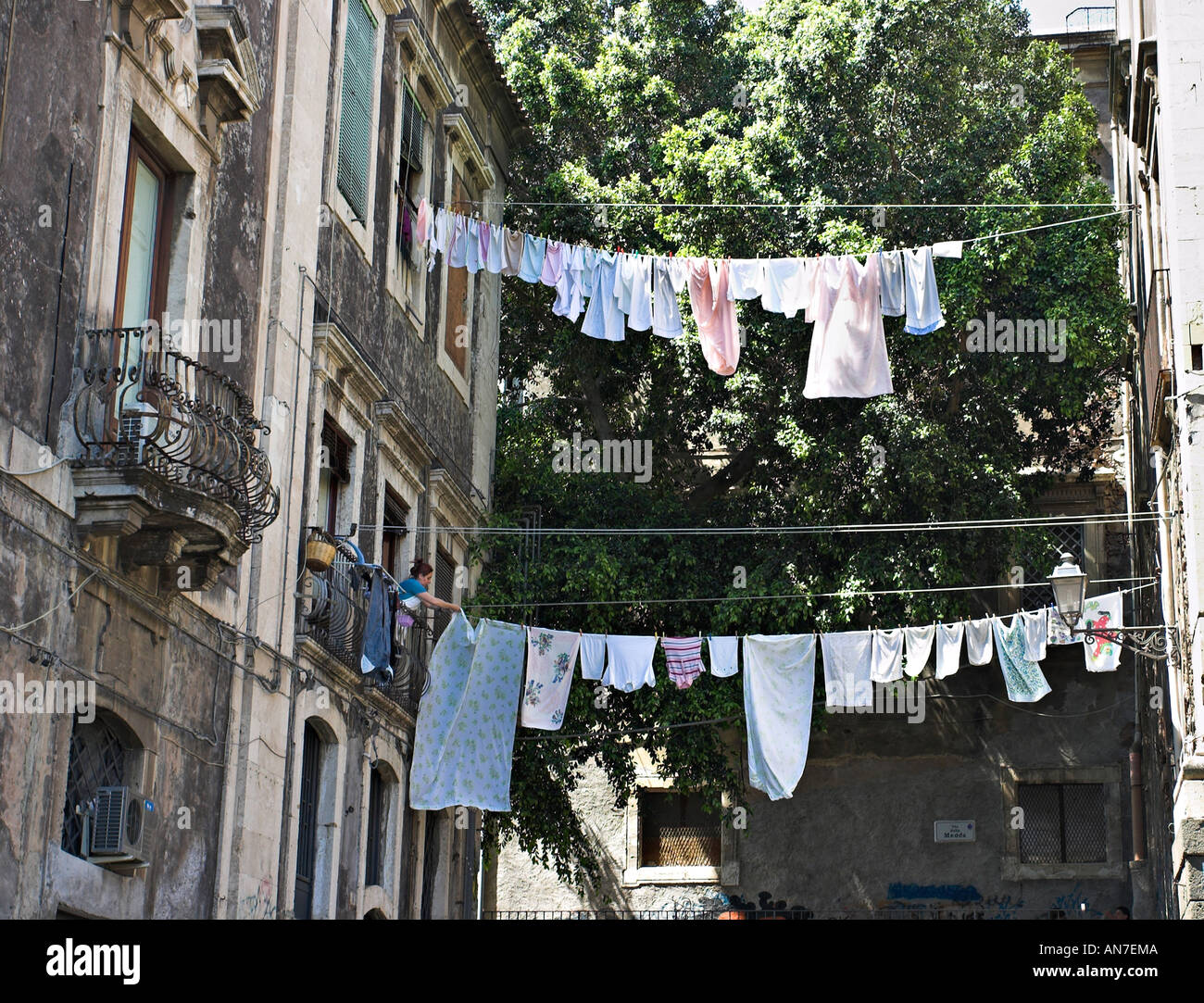 A woman puts out her washing between two historic buildings high above the street Stock Photo