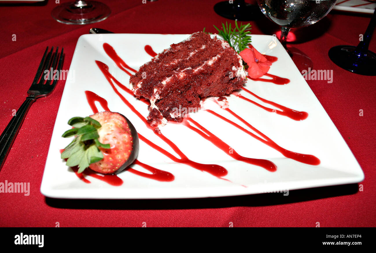 A raspberry Chocolate cake on a square white plate zig zagged with red and garnished with rosemary and a strawberry Stock Photo