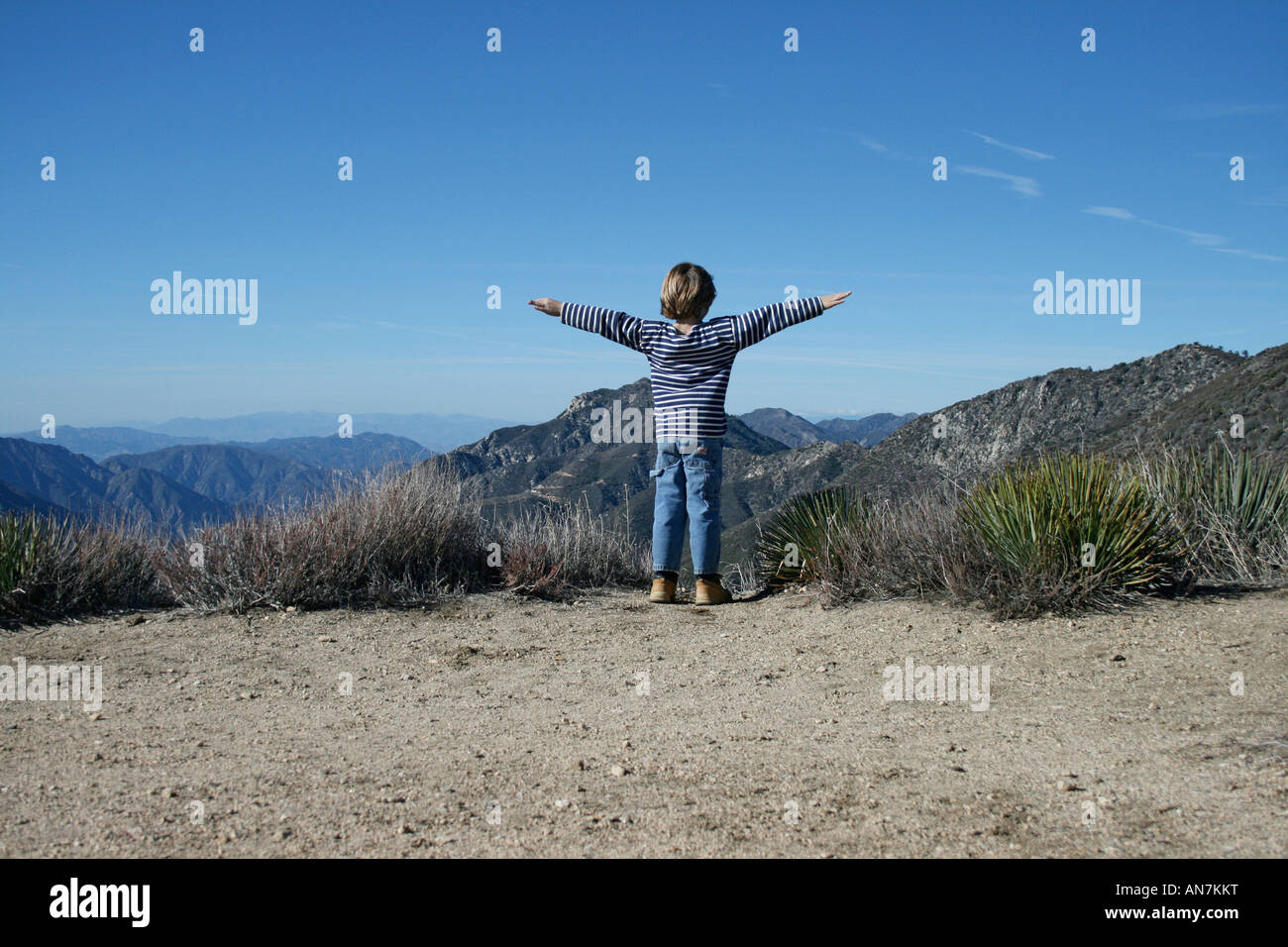 7 -9 year old boy in the desert mountains in California USA and puts his arms up to fly Stock Photo