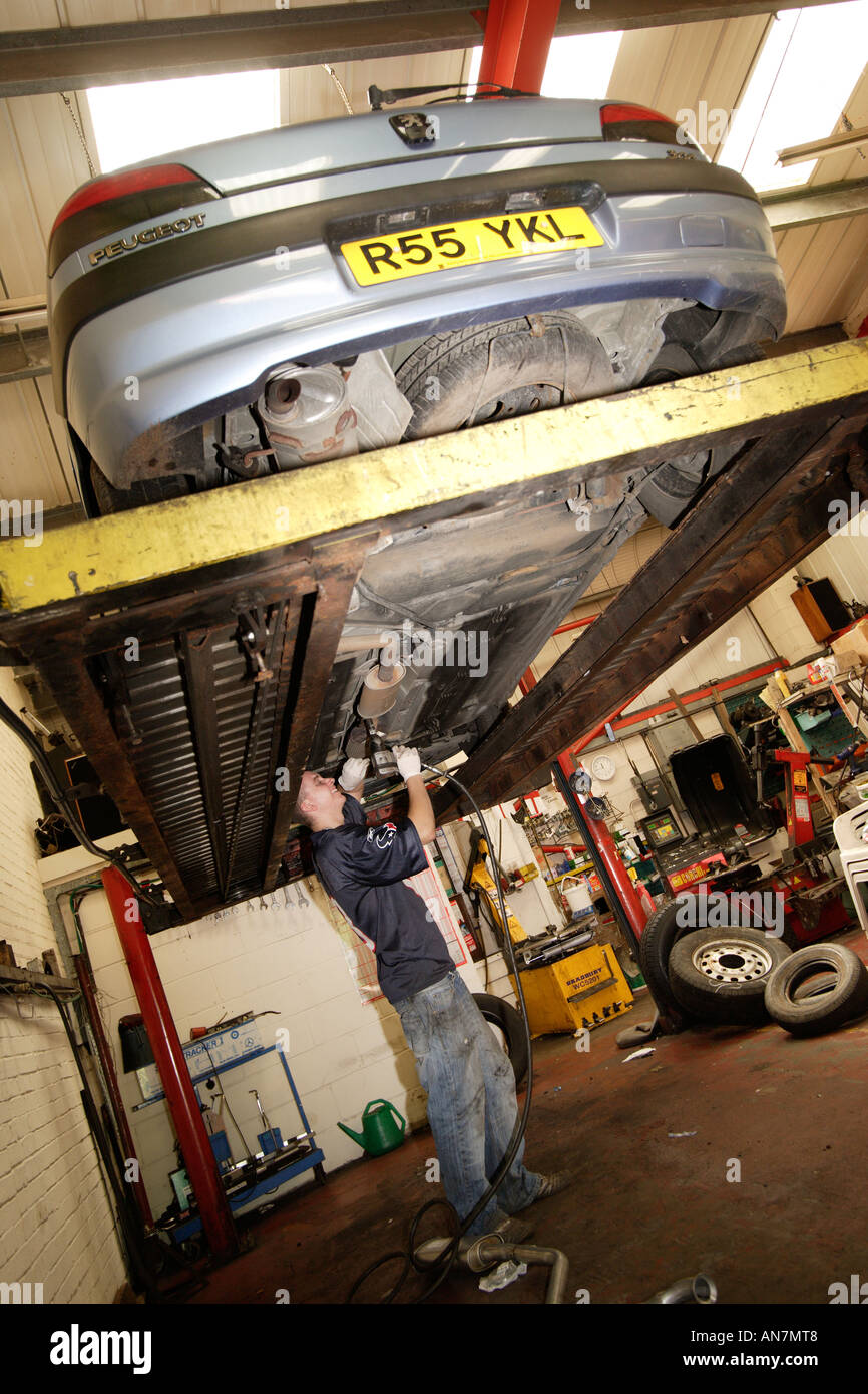 Car up on hydraulic lift at a garage Mechanic working underneath vehicle Stock Photo