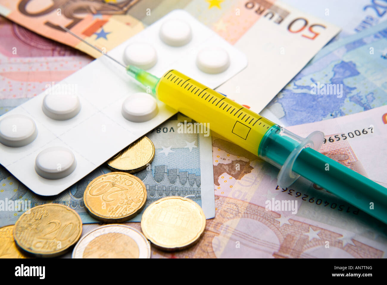 medical syringe filled with yellow liquid and white strip of pills lying on Euro bills and coins Stock Photo