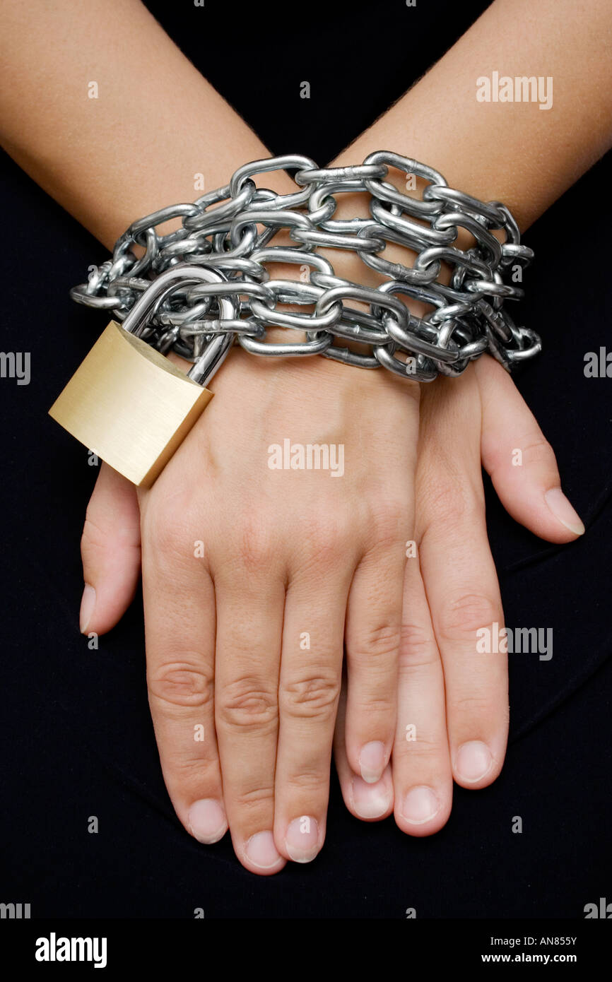 Female hands bound with chain and padlock. Isolated on a black background. Stock Photo