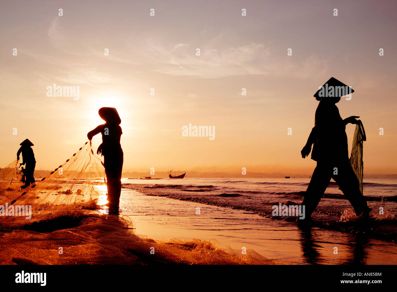 Three women in traditional hats on Mui Ne Beach, Vietnam Stock Photo