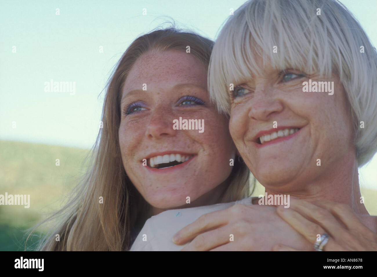 Portrait of 57 year old Caucasian woman with 22 year old daughter hugging her mother from behind Stock Photo