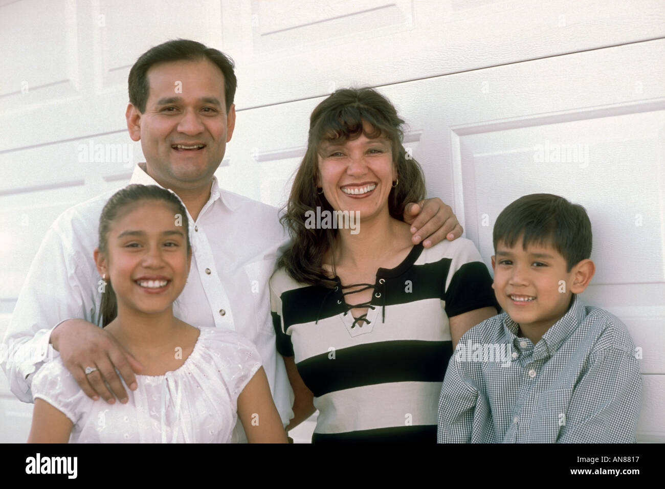 Portrait of Mexican family with 2 kids against white garage wall Stock Photo