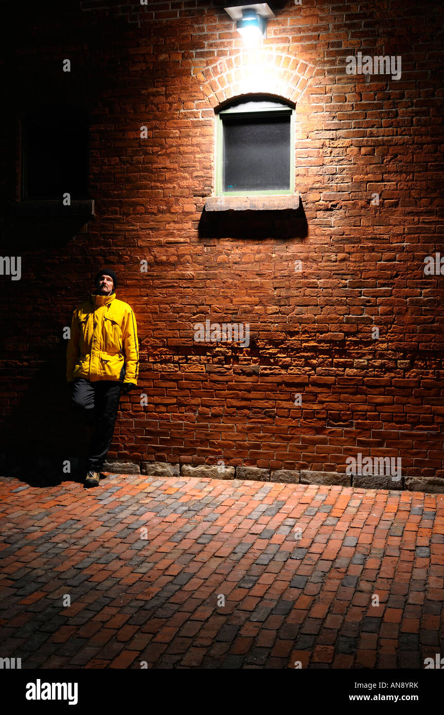 Single man leaning on a red brick wall under a streetlight on a cold
