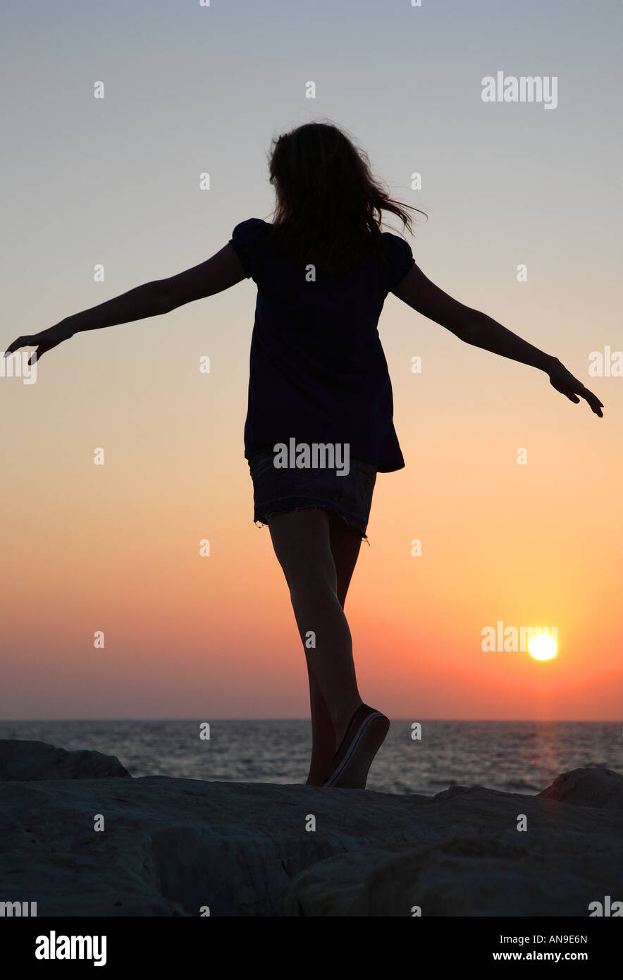 Teenage girl silhouetted against July sunset over the Mediterranean at ...