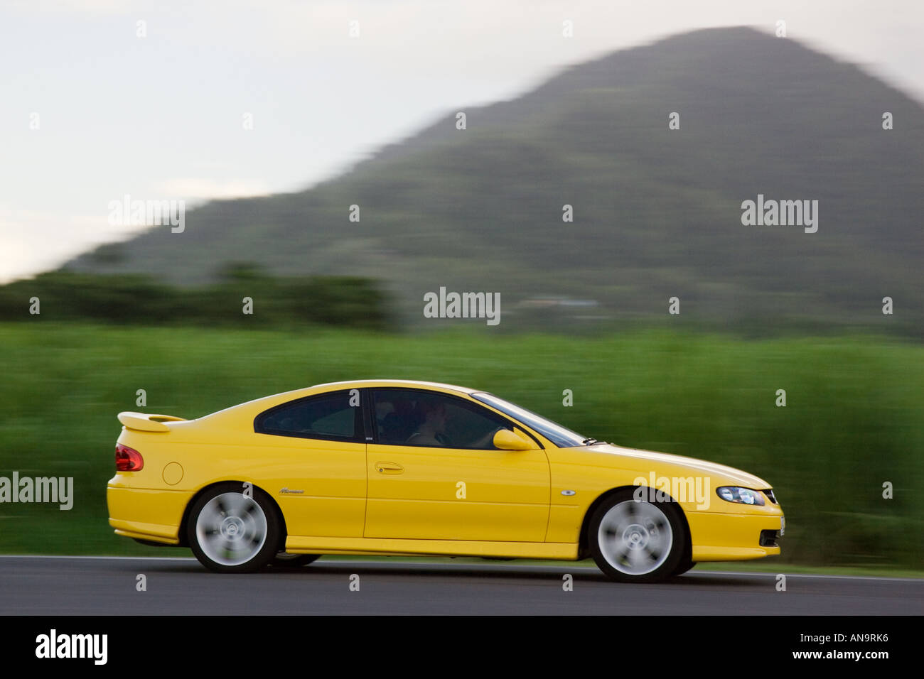 Holden Monaro car passes a sugar cane field at Freshwater Connection Australia Stock Photo