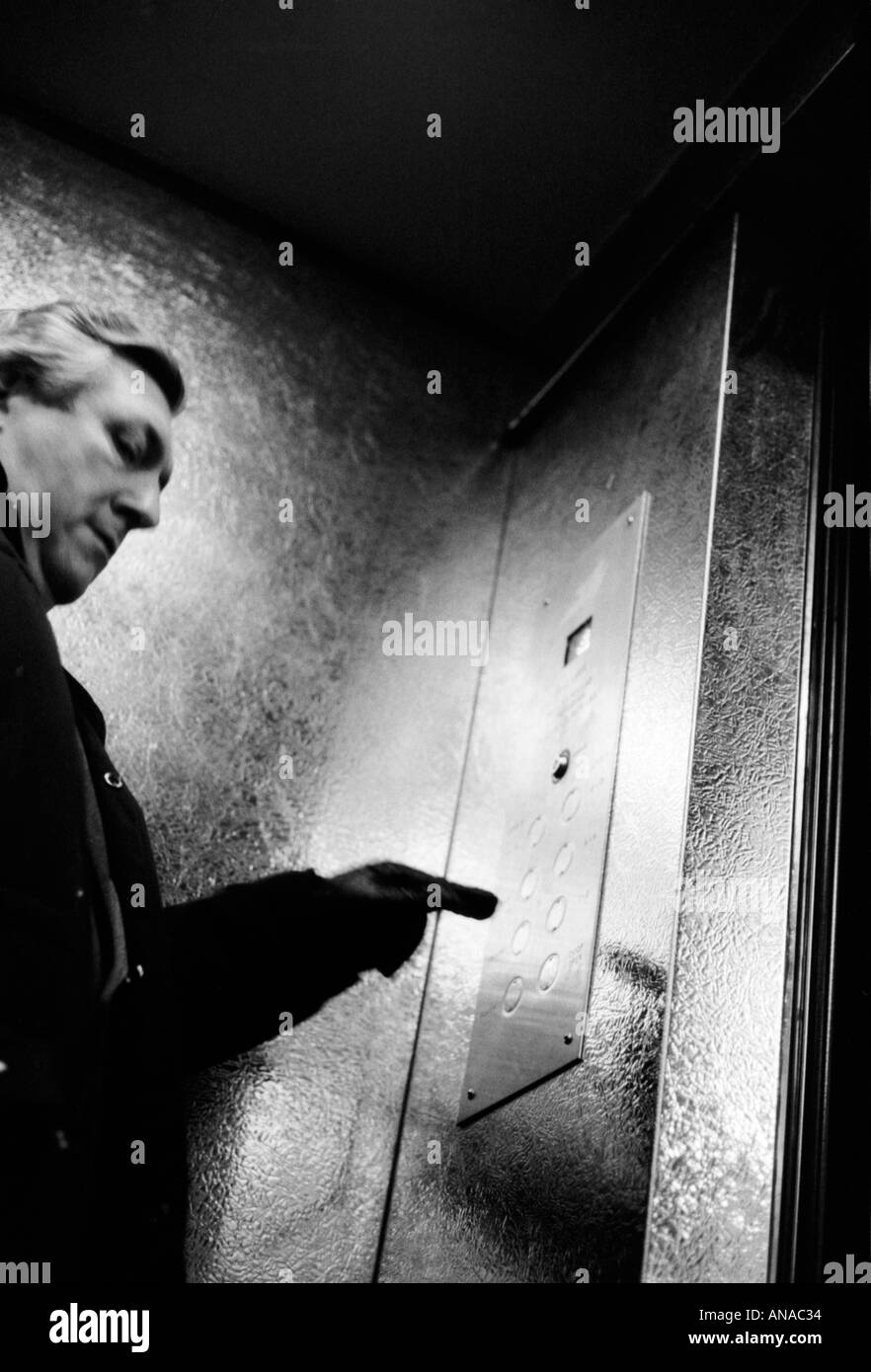 man in lift pressing a button shot in black and white Stock Photo
