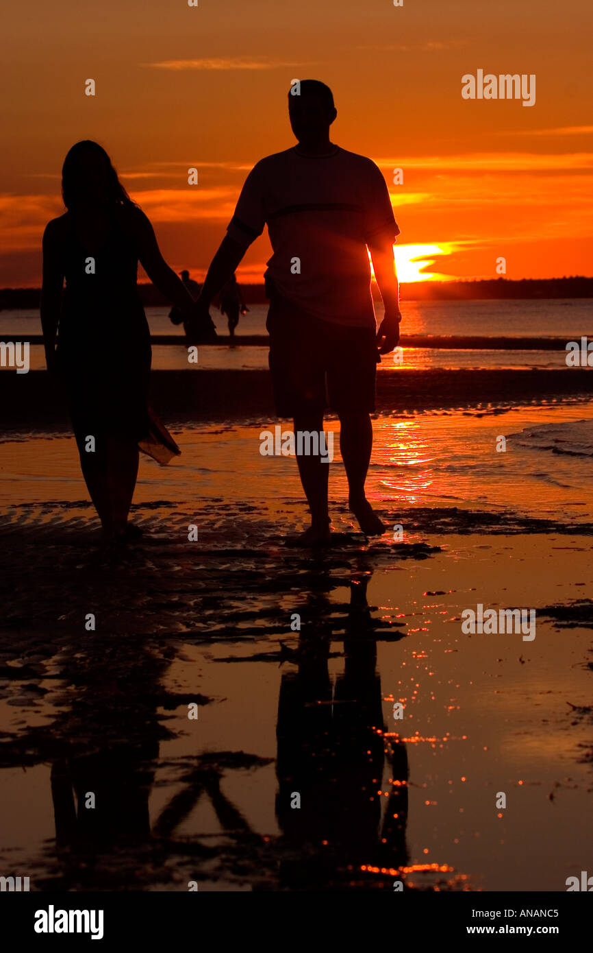 Silhouette of young couple walking on beach at sunset Stock Photo - Alamy