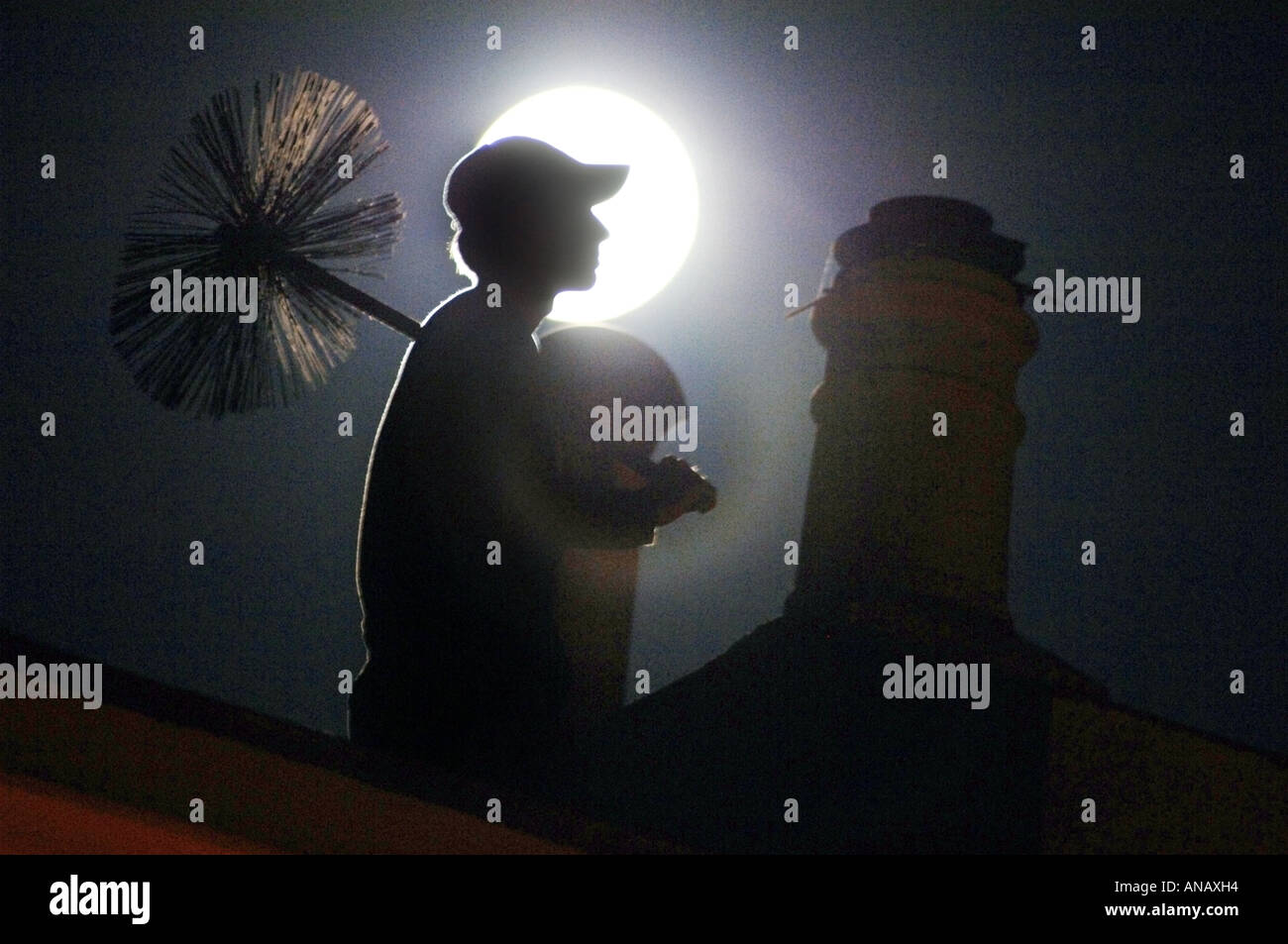 The misty figure of a young chimney sweep on a rooftop under a full moon Stock Photo