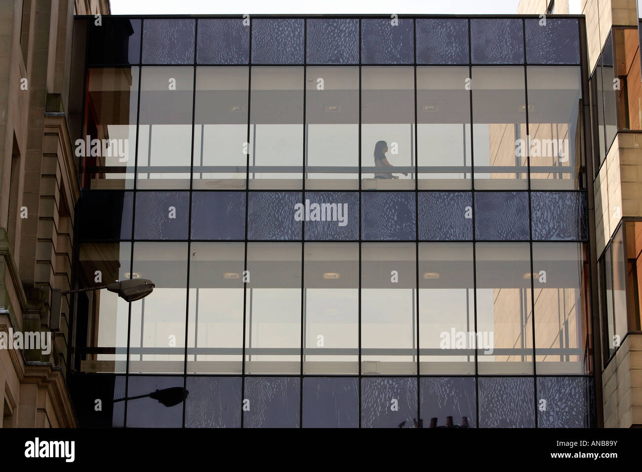 A WOMAN WALKING ALONG A GLASS COVERED WALKWAY BETWEEN TWO BUILDINGS. Stock Photo