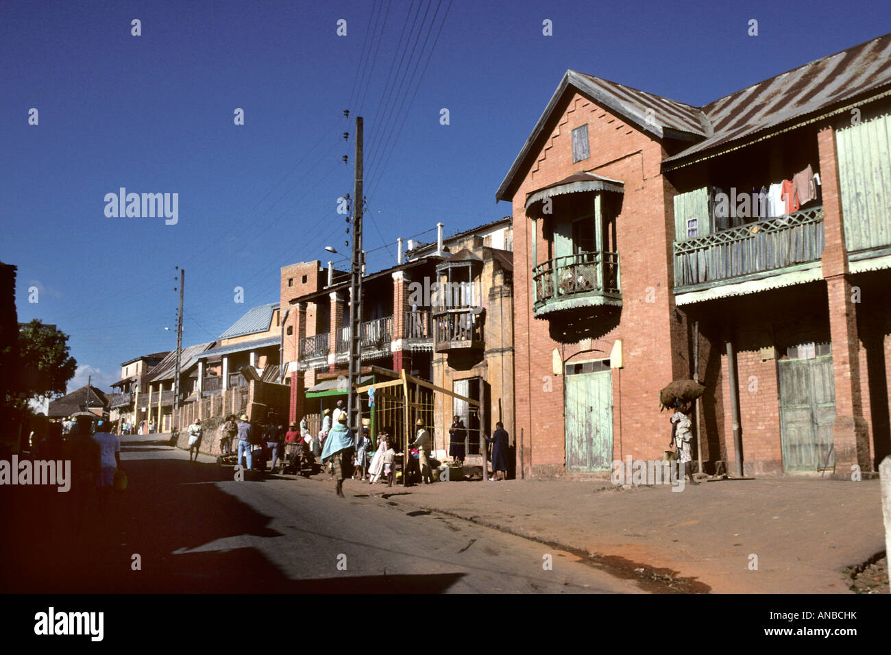 Street scene in Ambositra showing a row of houses and people walking down the street Stock Photo