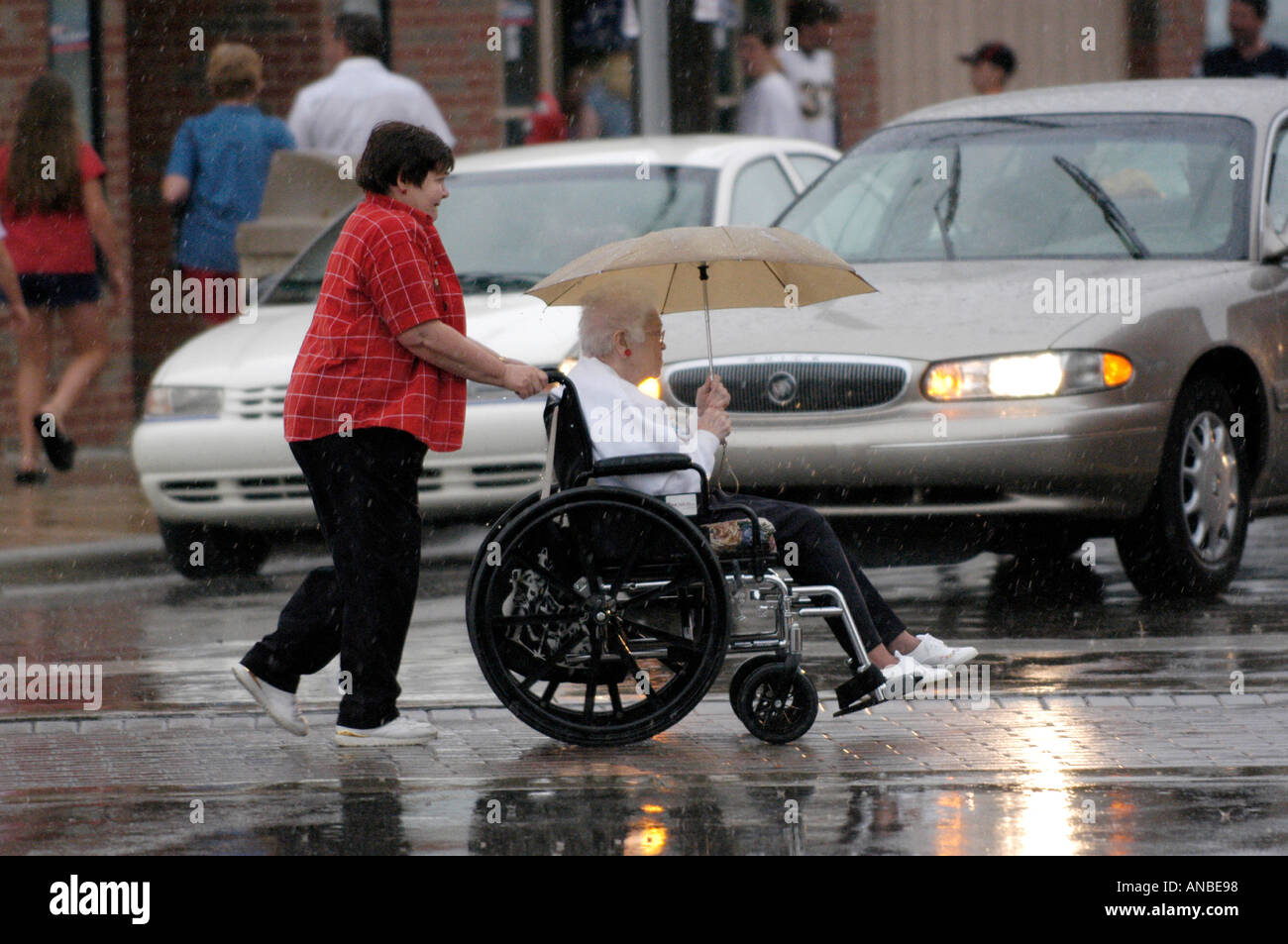 Daughter Pushes Elderly Senior Mother in Wheelchair in Rain Stock Photo