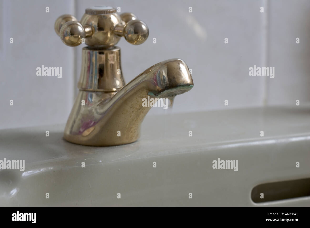 Dripping gold tap wasting water in bathroom UK Stock Photo