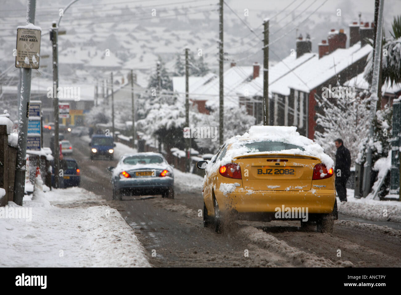 cars driving downhill slowly along slush covered road wheels spinning