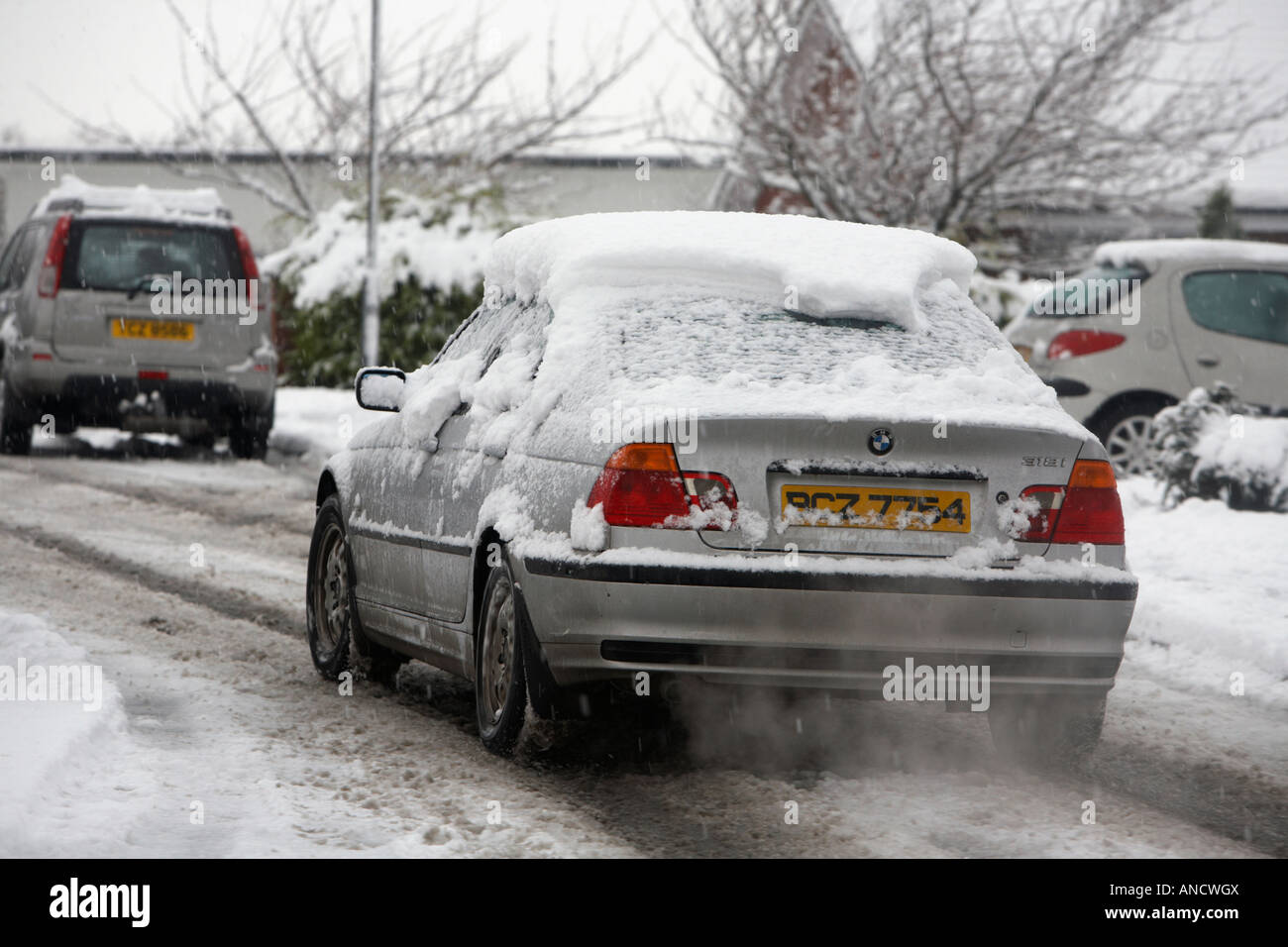 BMW 3 series covered in snow drives slowly along untreated street