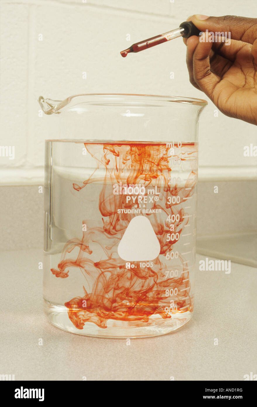 Red dye being dispersed by dropper in beaker of water, African American