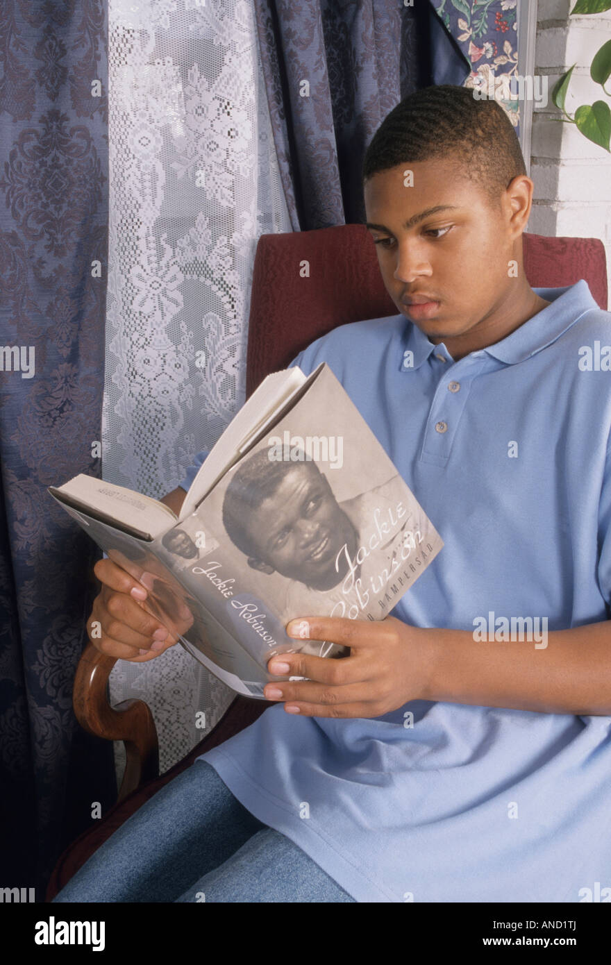 Teen reads book in home setting, homework education leisure time Jackie Robinson biography African American black teen male Ohio Stock Photo