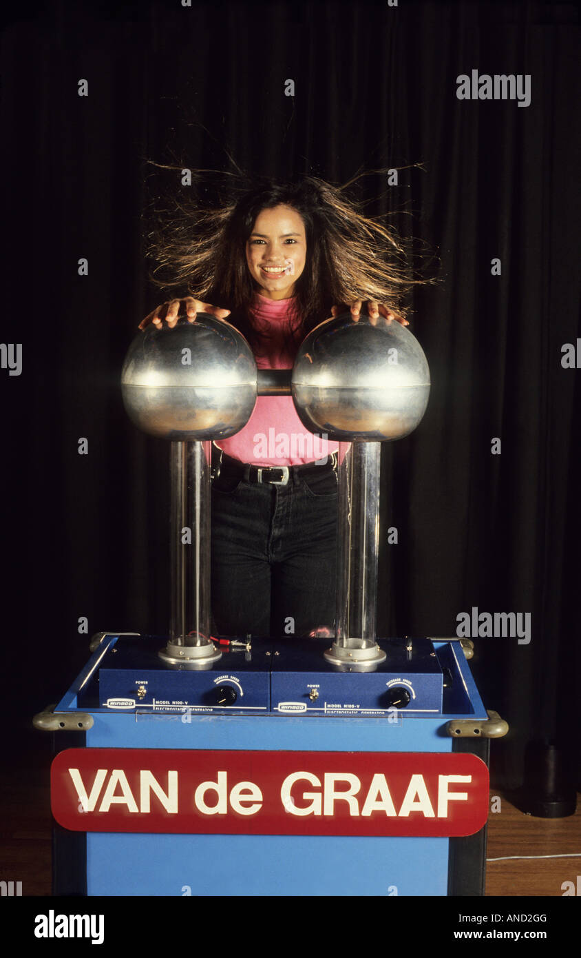 Hair stands up while teen touching Van de Graaf meter, Hispanic female teen student, static electricity. Stock Photo