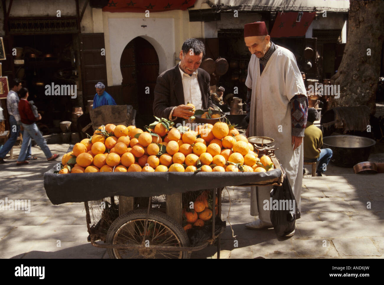 Orange seller wearing djellaba, customer at Place as Seffarine Kairaouine Quarter Medina Fez Morocco Stock Photo