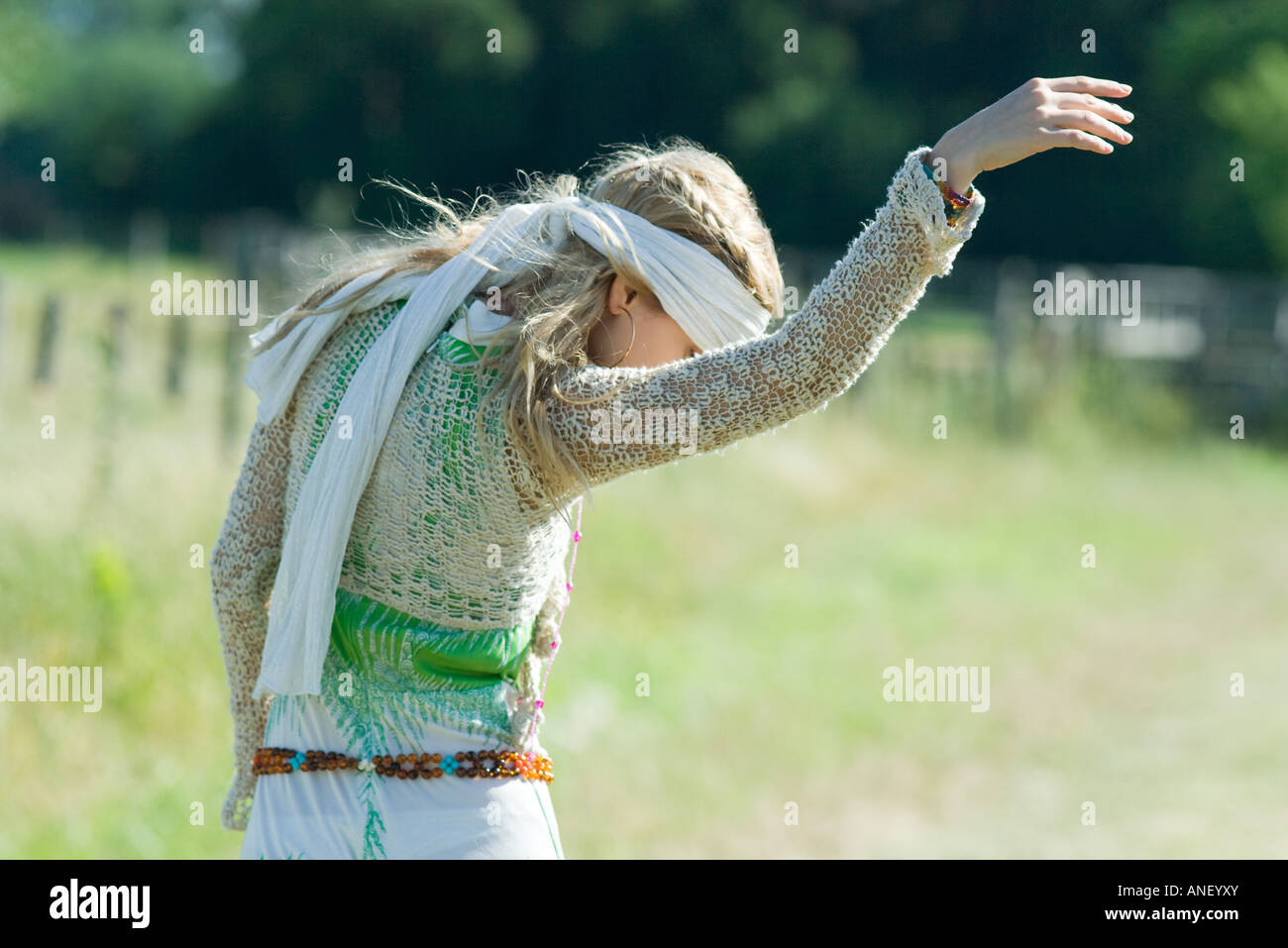 Young woman in sundress standing in field with arm up, looking down Stock Photo