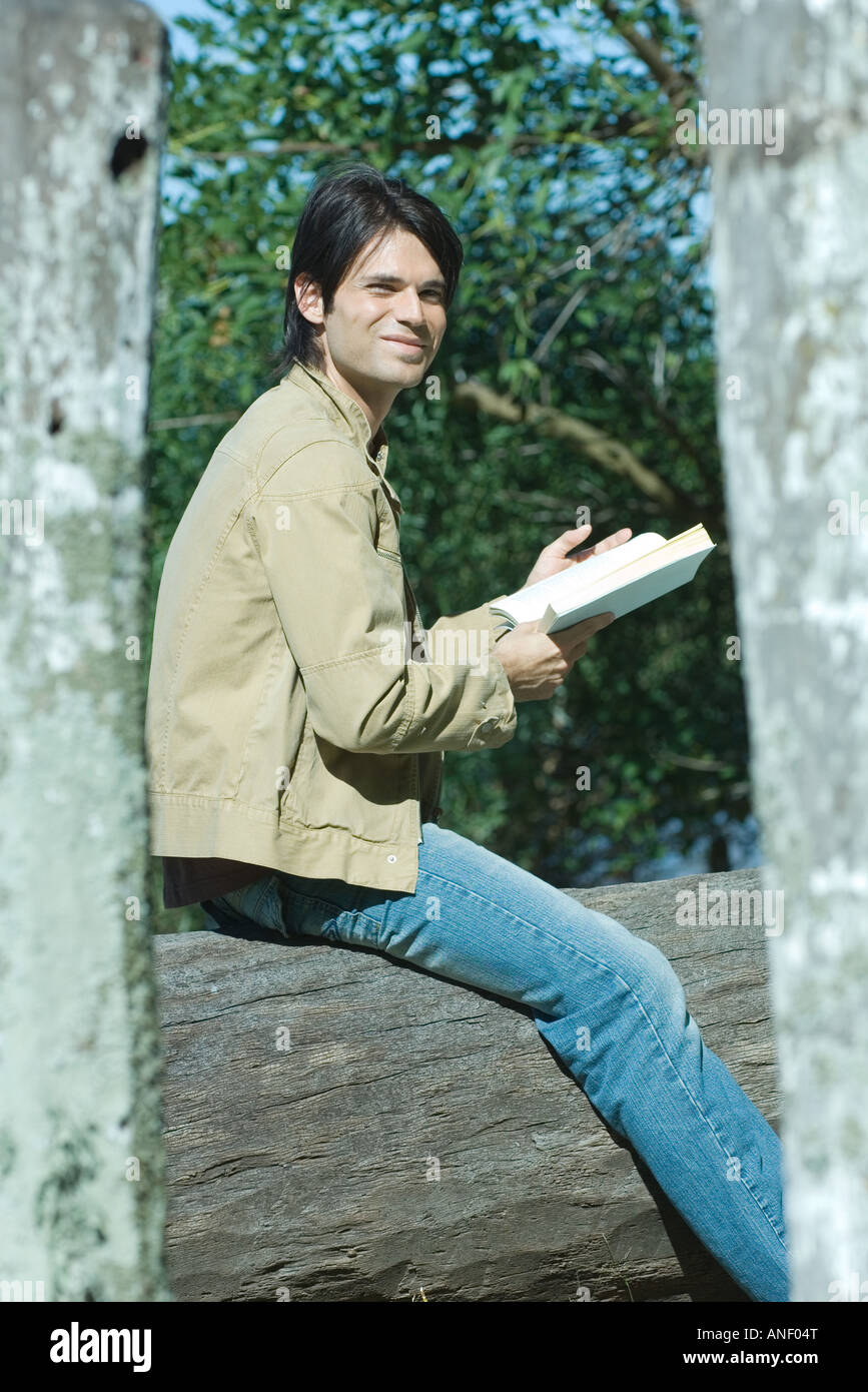Man sitting on tree trunk outside, reading book Stock Photo