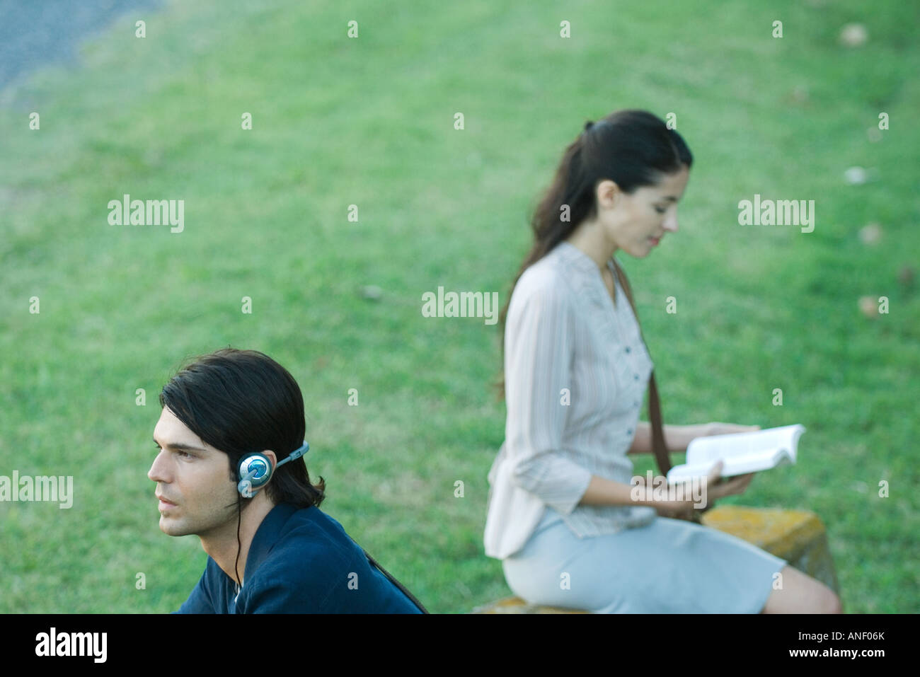 People sitting in park, man listening to headphones while woman reads book Stock Photo