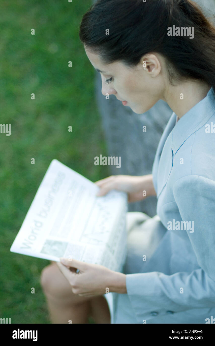 Businesswoman sitting on bench, reading newspaper Stock Photo