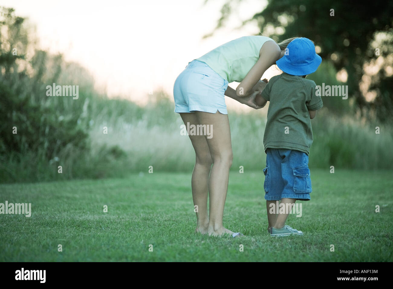 Mother and son standing on lawn, woman bending over to talk to boy Stock Photo