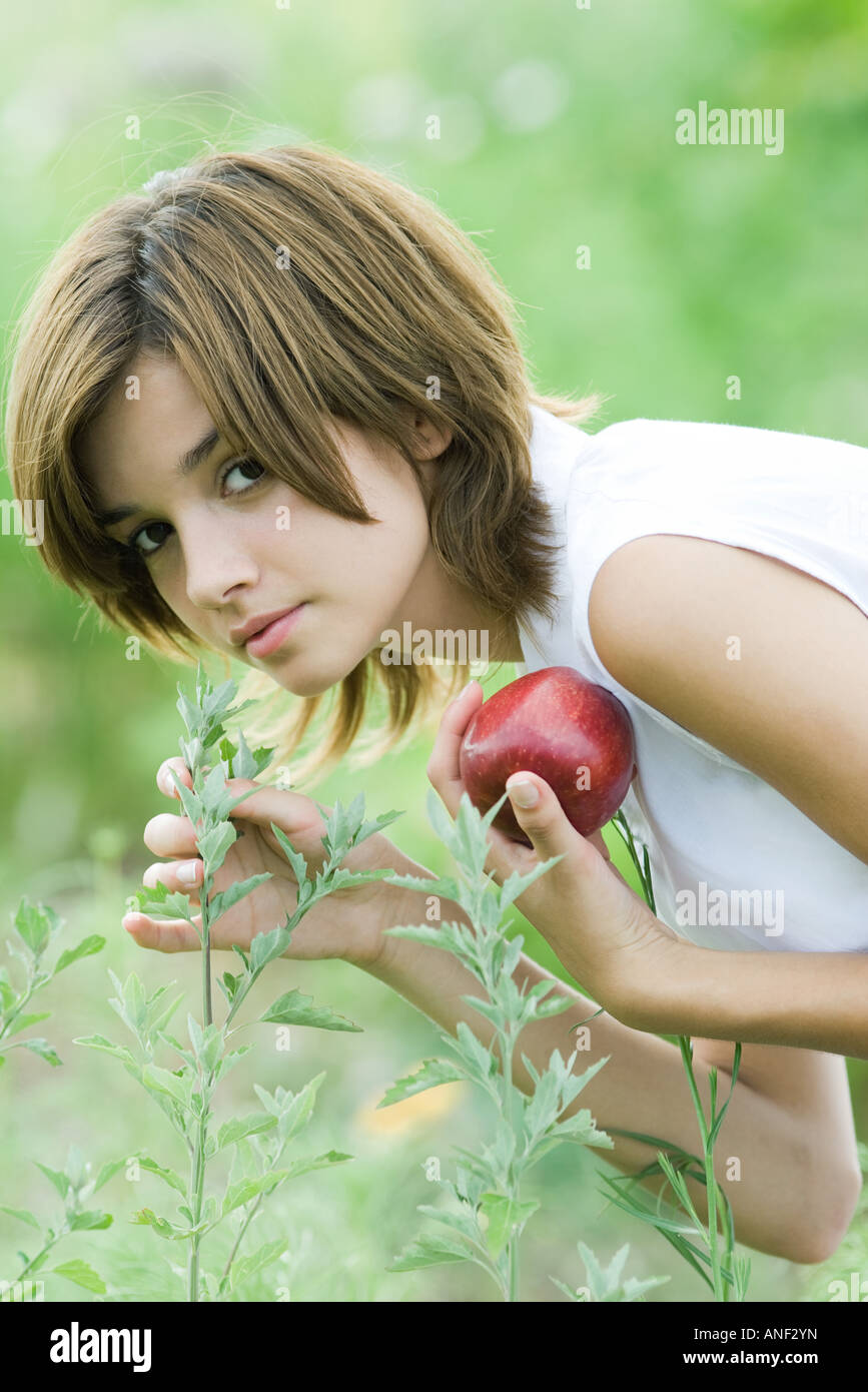 Young woman smelling plant, holding apple Stock Photo