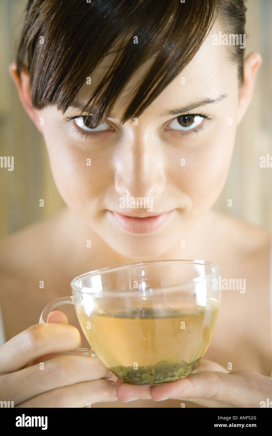 Young woman holding cup of herbal tea, looking at camera, close-up Stock Photo