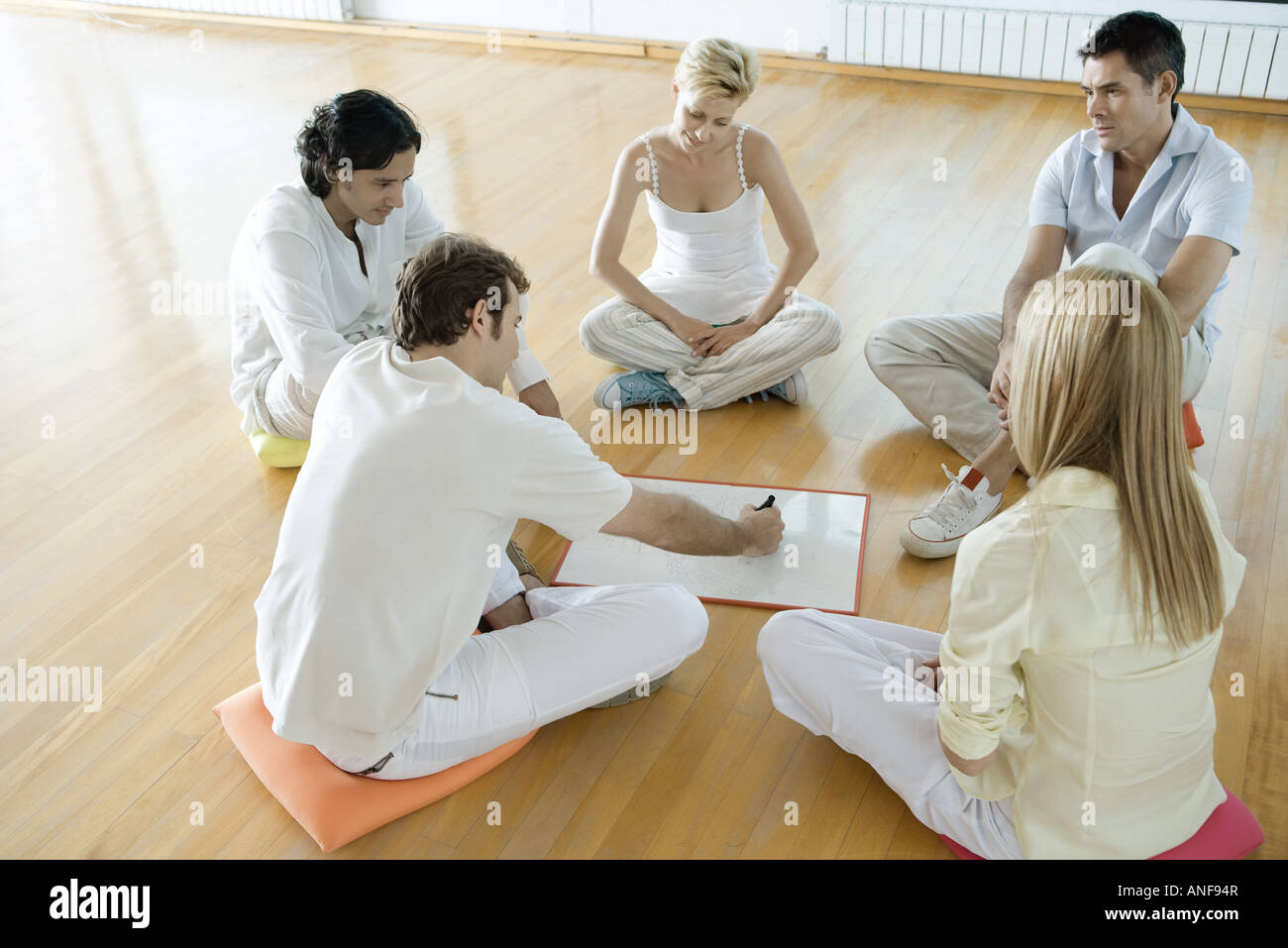 Group of adults sitting on cushions on floor, one man drawing on